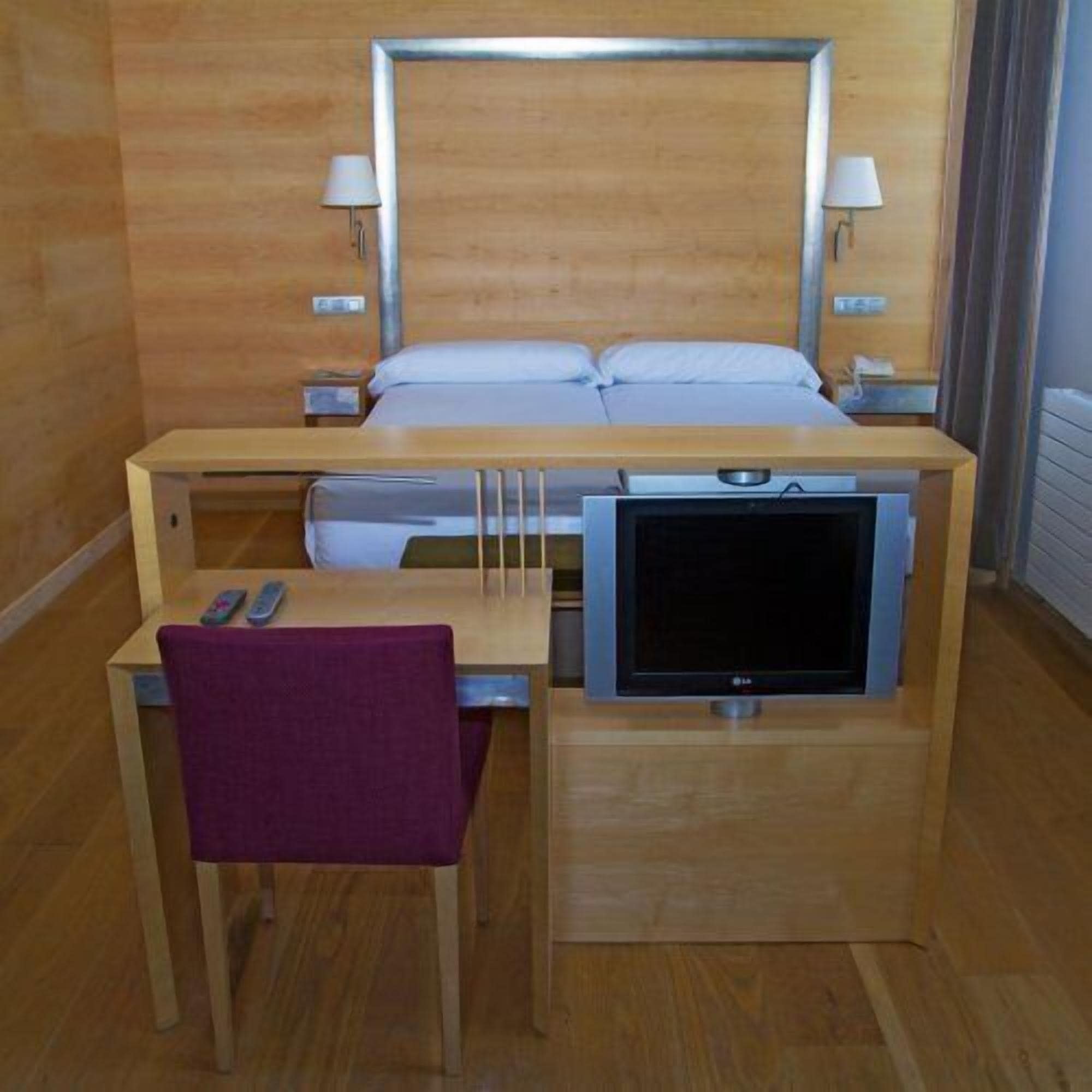 A hotel room with a bed, bedside lamps, a TV, a desk, and a chair.