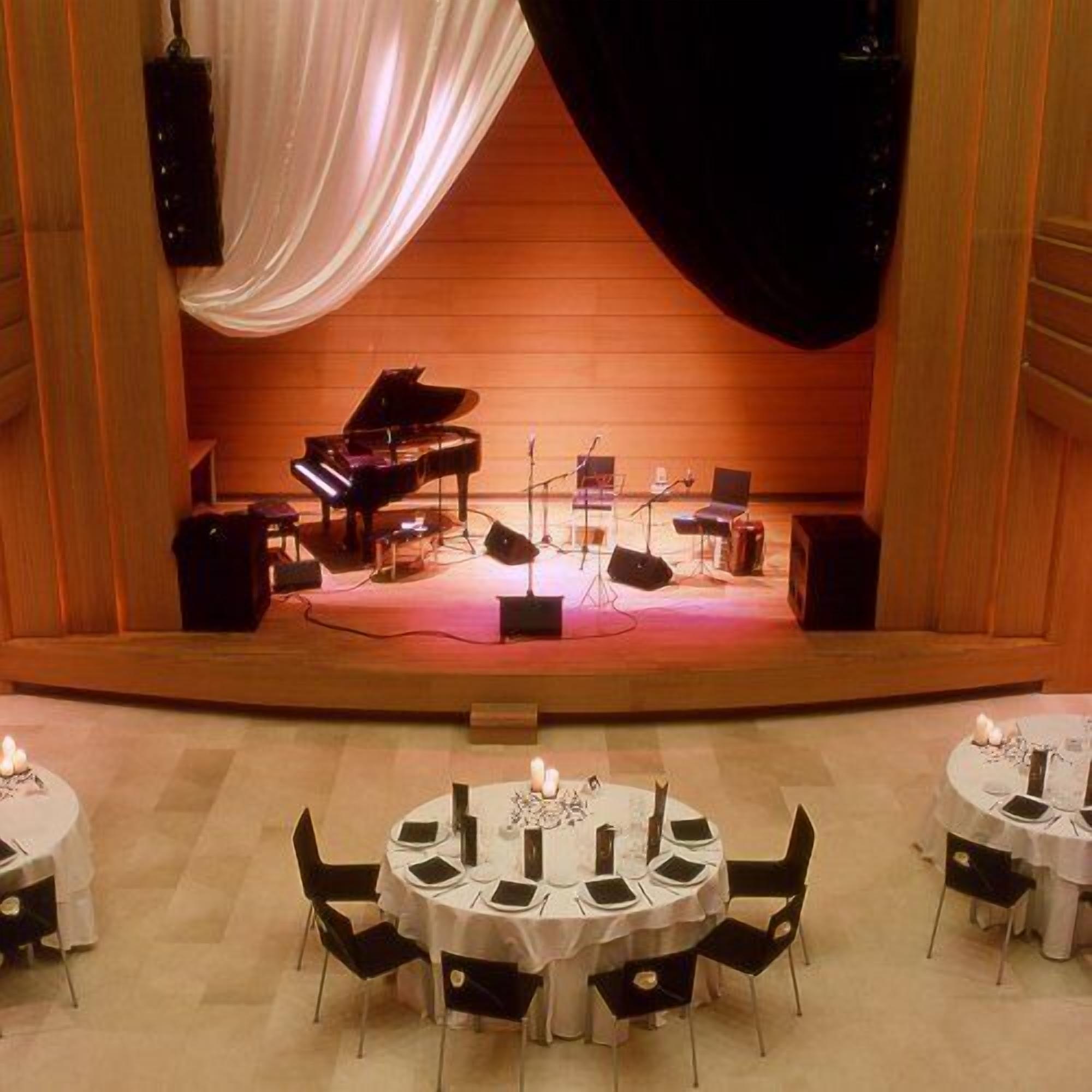 A stage with a grand piano and a piano bench, surrounded by musical instruments and microphones.