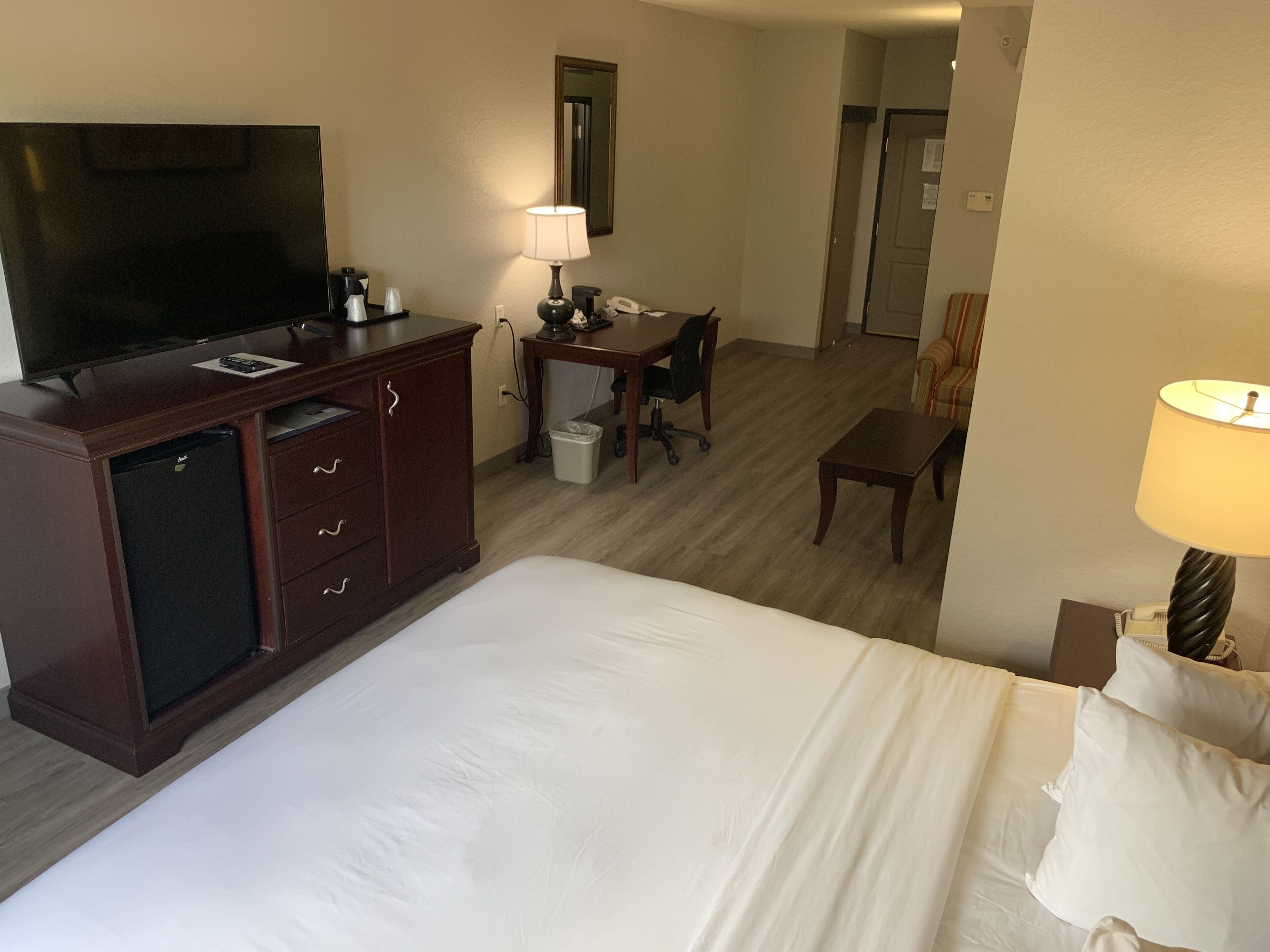 Een hotelkamer met een bed, een bureau, een stoel, een televisie, een lamp en een minibar.