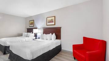 Habitación de hotel con dos camas, un sillón rojo, un cabecero de madera y dos cuadros enmarcados en la pared.