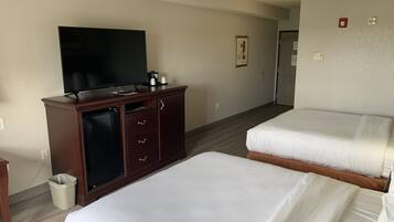 Habitación de hotel con dos camas, televisión, minibar y un cubo de basura.