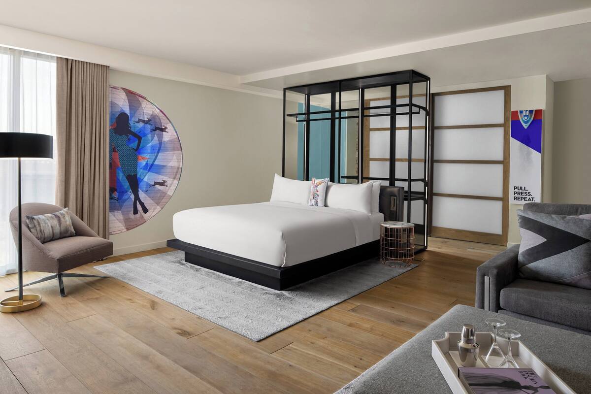 Un dormitorio moderno con una cama grande, una mesita de noche, una silla, una lámpara de pie y un adorno en la pared.