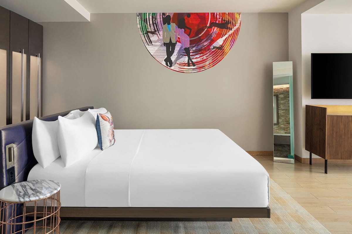 Una habitación de hotel moderna con una cama grande, un televisor y una pieza de arte única en la pared.