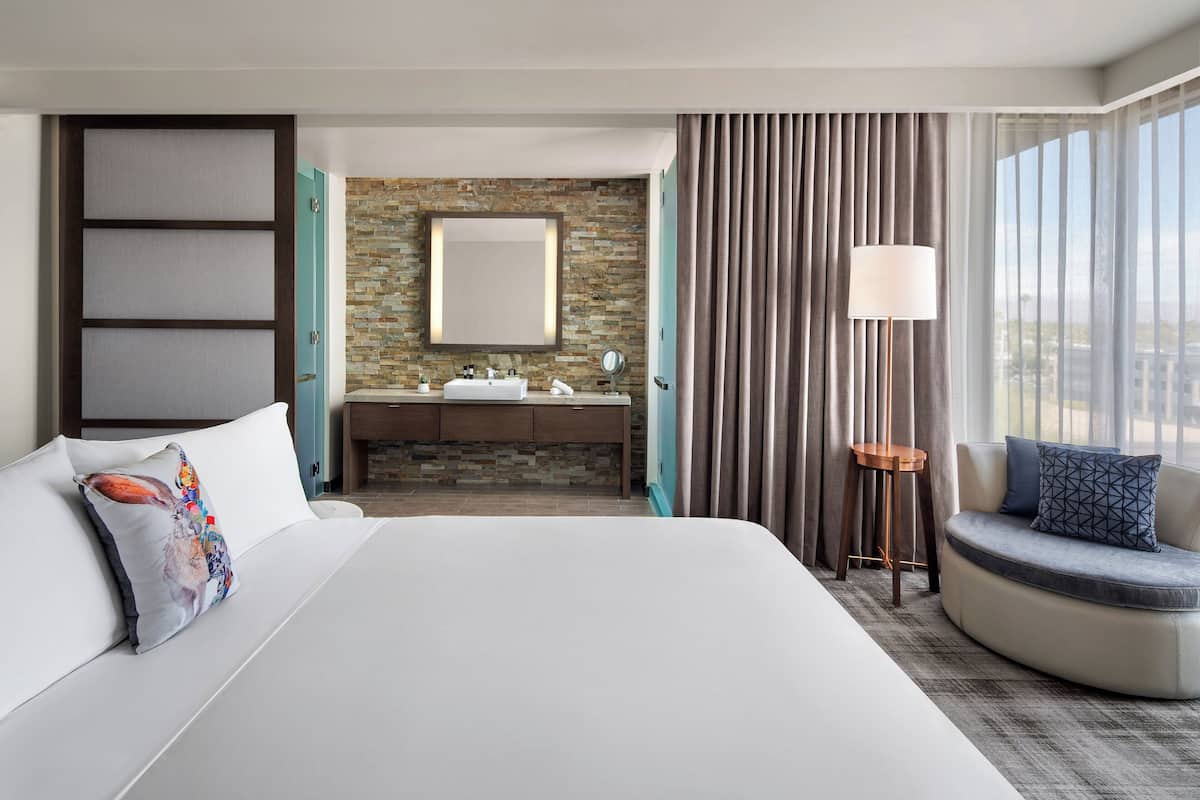 Habitación de hotel con una cama grande, baño con pared de piedra, zona de estar circular y vista por la ventana.