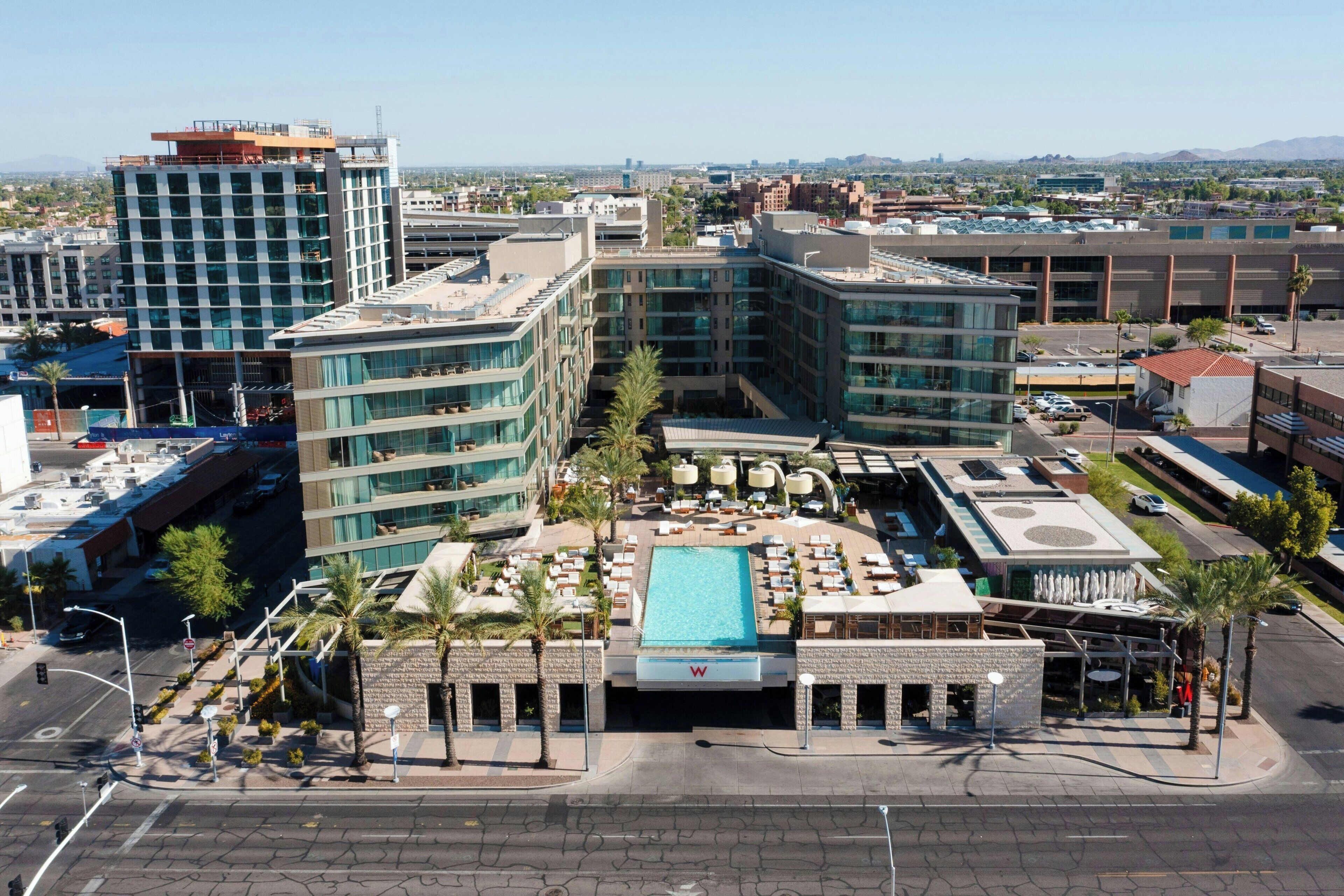 A hotel with a rooftop pool, multiple floors, and a view of the surrounding cityscape.