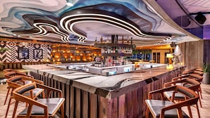 A bar area with a central island, wooden chairs, and a ceiling with a wavy light design. - W Scottsdale (Scottsdale)