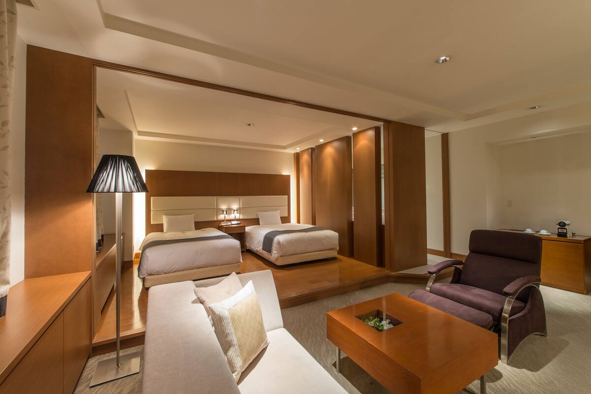 A modern hotel room with a large bed, a sofa, a desk, and a chair.