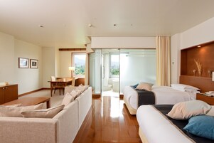A hotel room with a sofa, two beds, a desk, and a view of the outdoors.