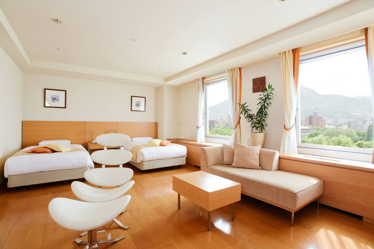 A modern hotel room with a bed, sofa, chairs, and a coffee table.