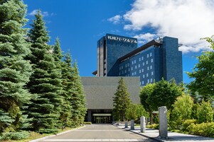 A modern building with a prominent sign, surrounded by evergreen trees and a clear sky.