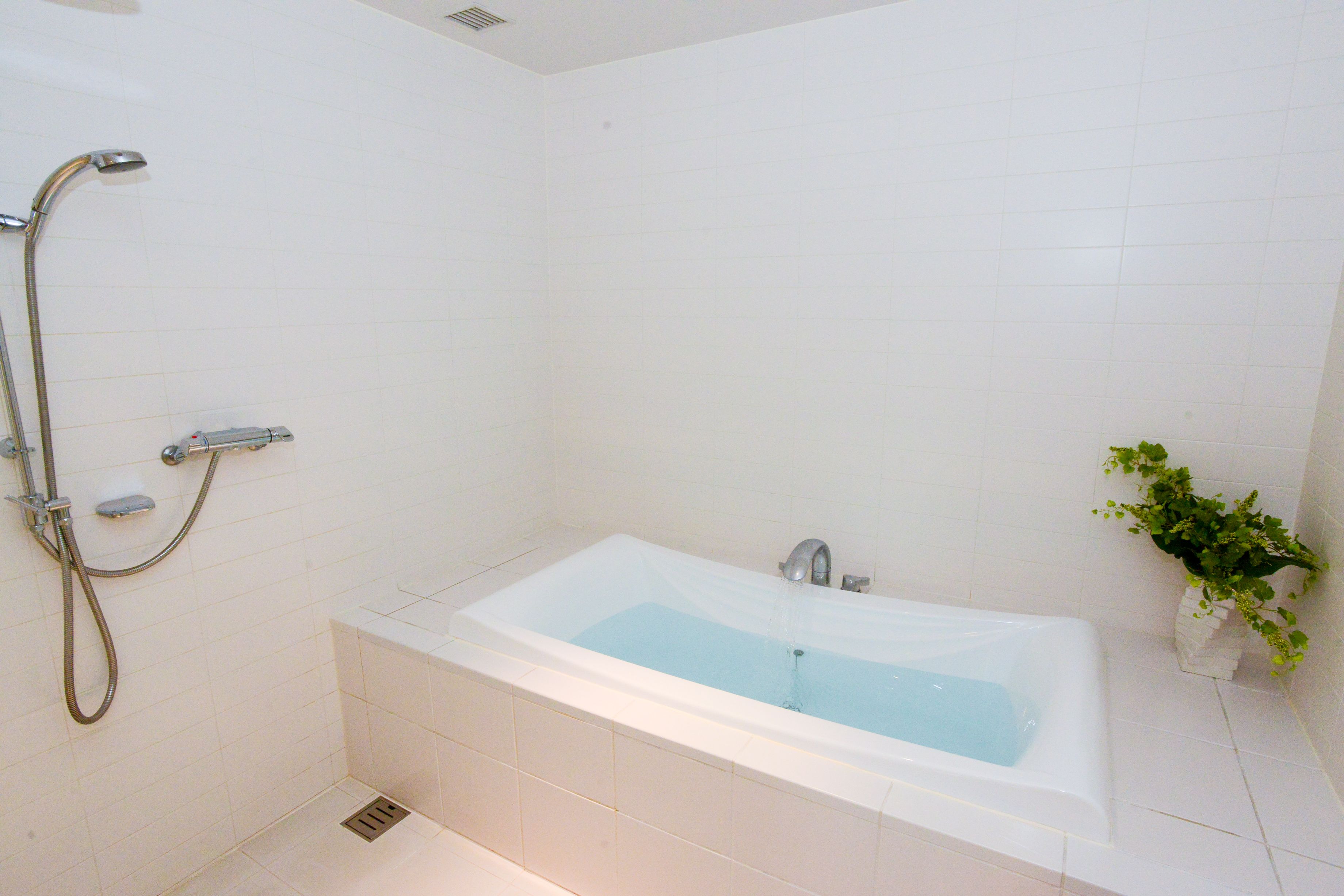 Un baño moderno con una bañera independiente, un cabezal de ducha manual y una pequeña planta en maceta.