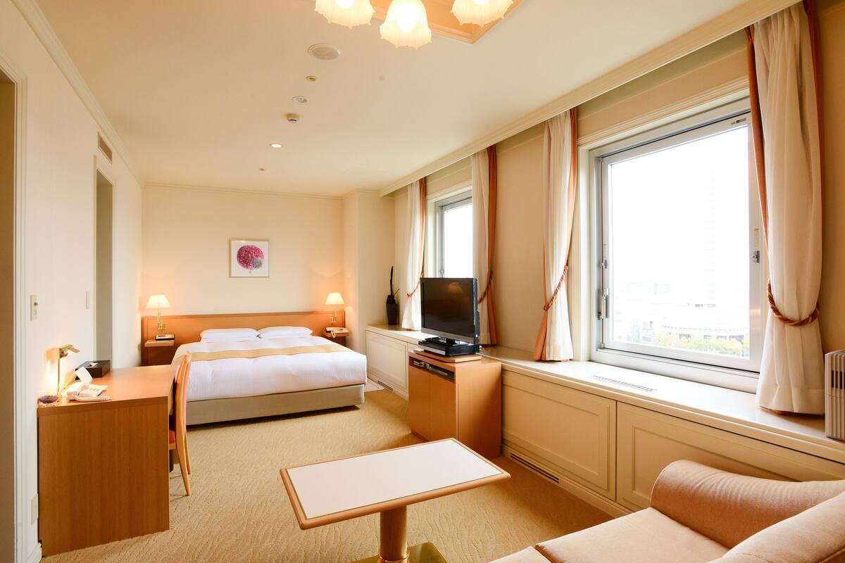 A hotel room with a bed, a desk, a television, and a window with curtains.