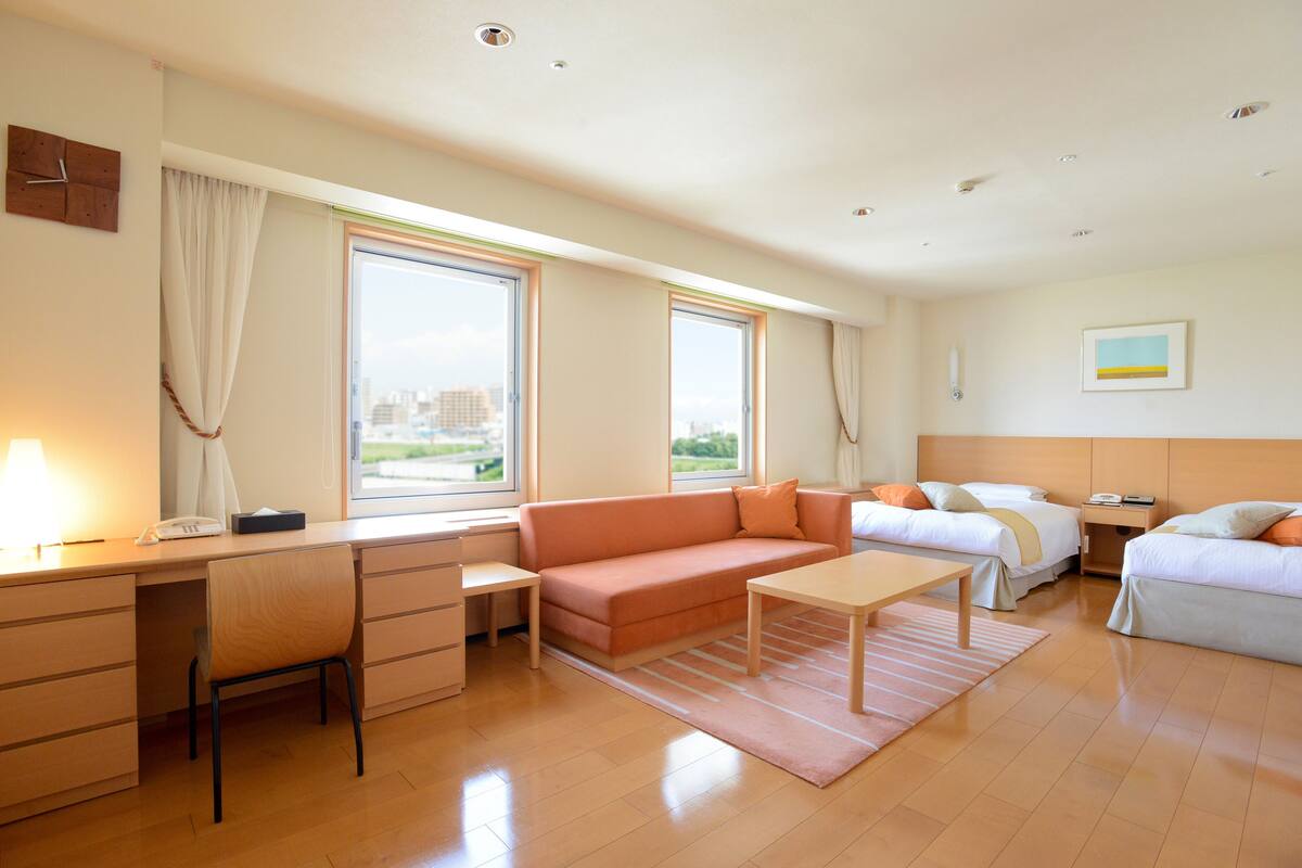 A modern hotel room with a desk, sofa, and two beds.