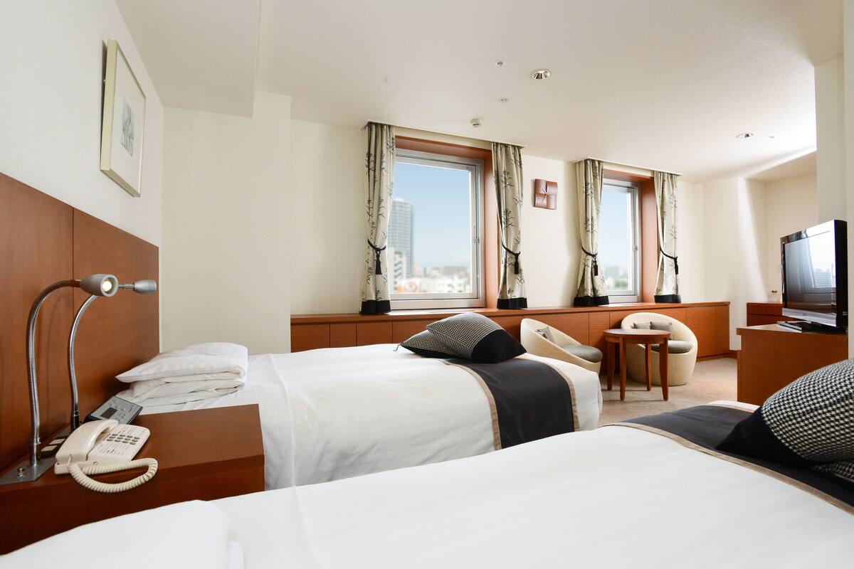 A hotel room with two beds, a desk with a telephone, a television, and a window with curtains.