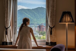 A room with a large window, curtains, a lamp, and a view of a mountain and buildings.