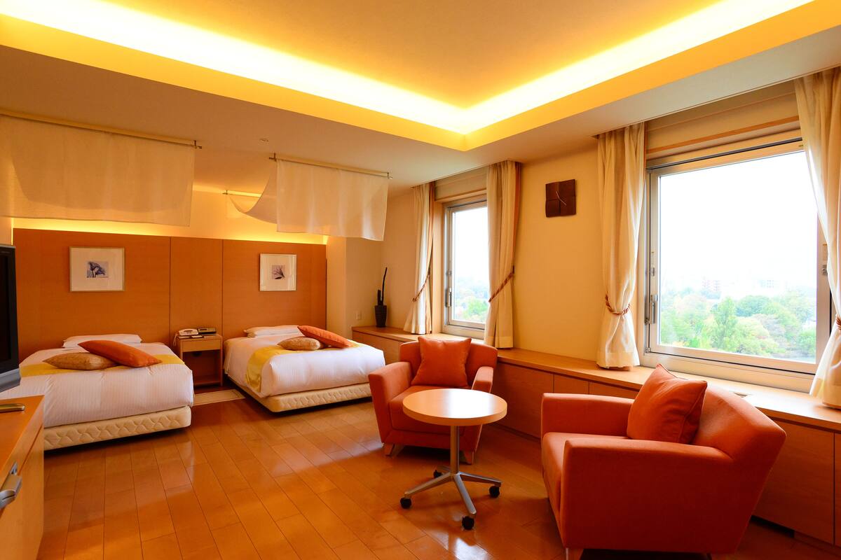 A hotel room with two beds, a desk, a chair, and a small table.