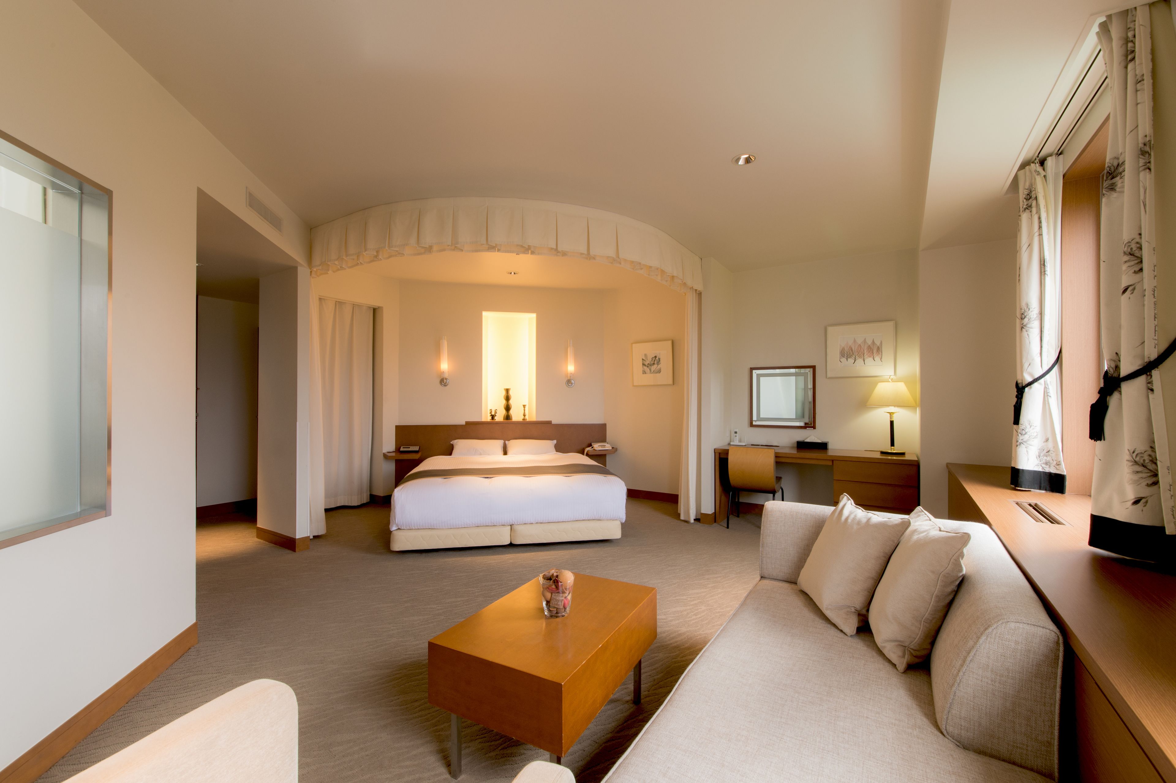 A hotel room with a bed, a sofa, a coffee table, a desk, and a TV.