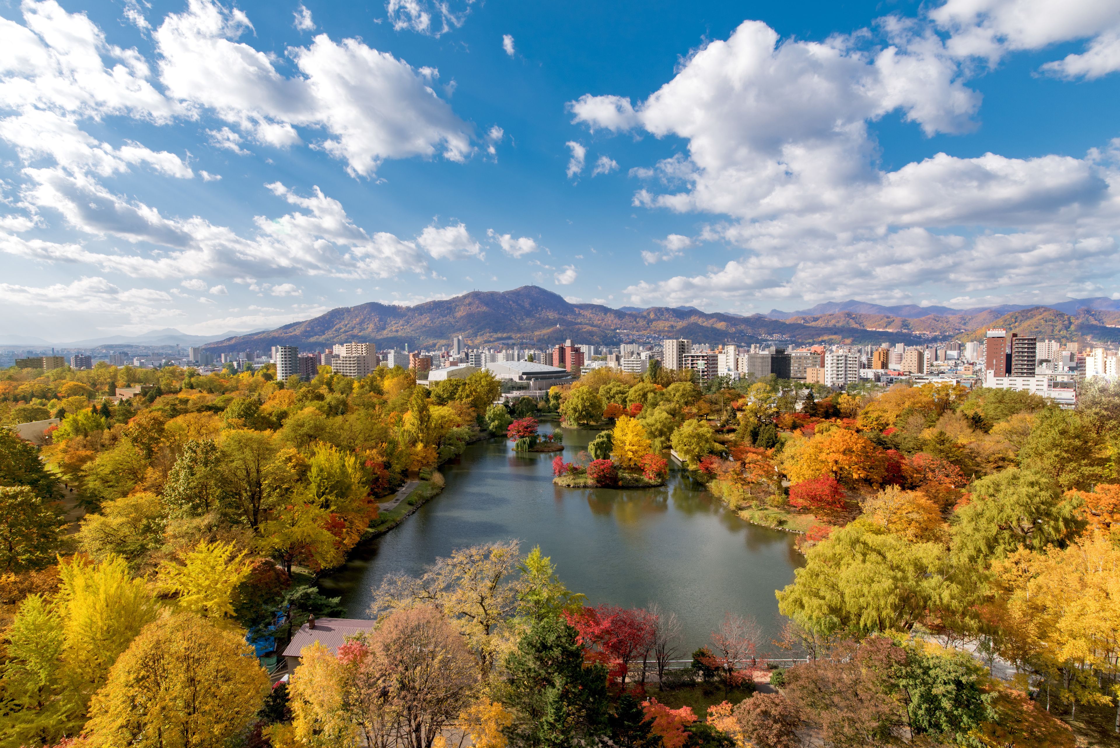 A cityscape with a river, autumn foliage, and mountains in the background.
