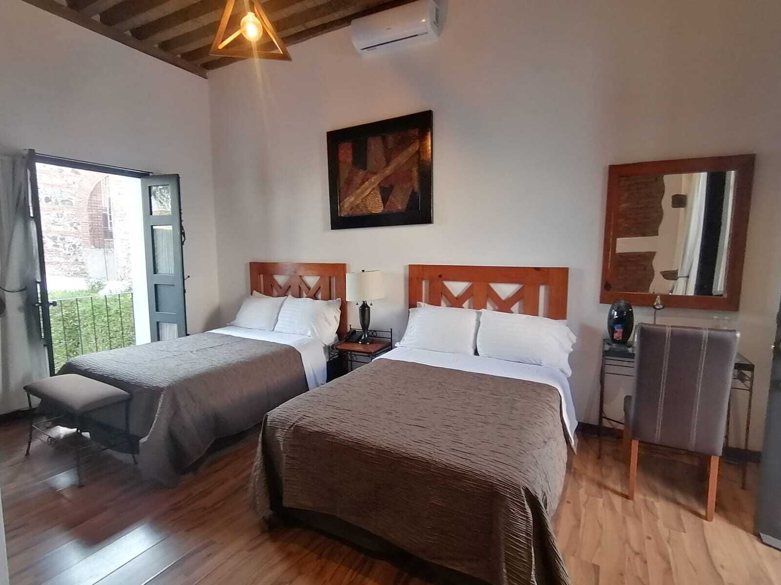 Habitación de hotel con dos camas, techo de madera, un cuadro en la pared y un espejo.