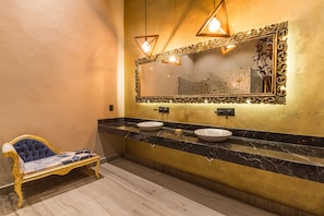 Relax in this elegant bathroom with a large mirror, two sinks, and a tufted sofa.