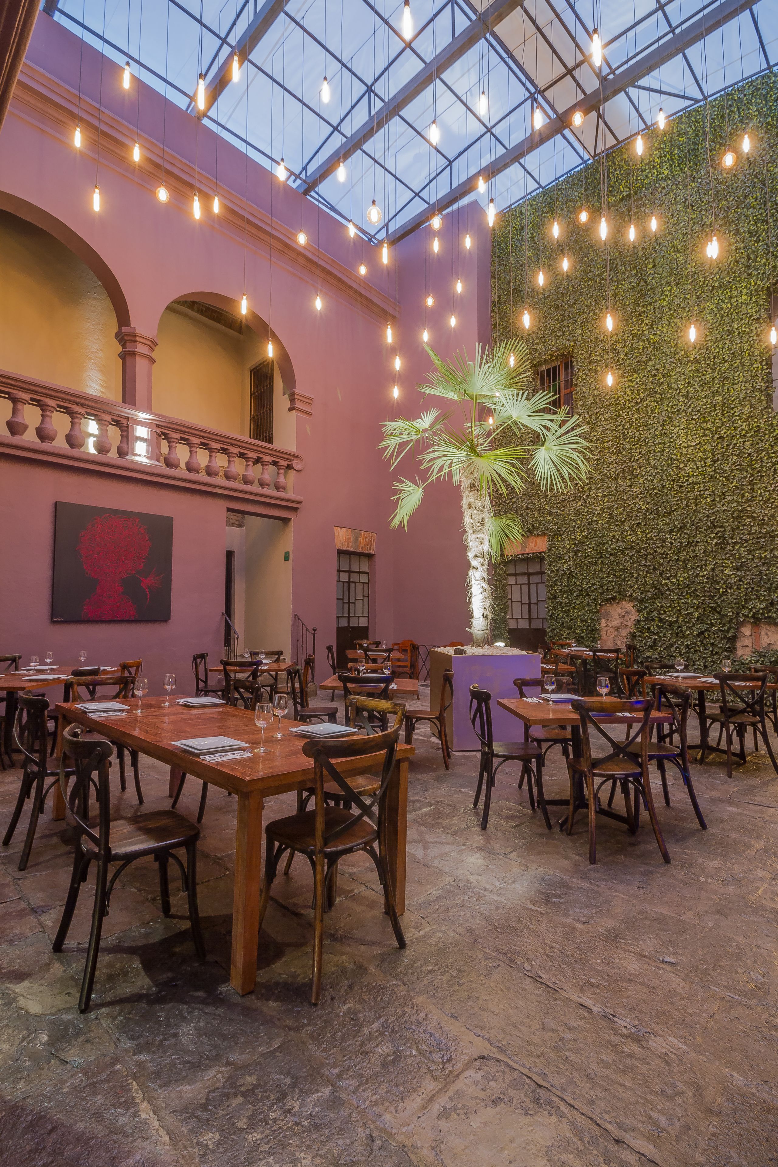 An indoor dining area with tables and chairs, a large potted plant, and a wall covered in greenery.