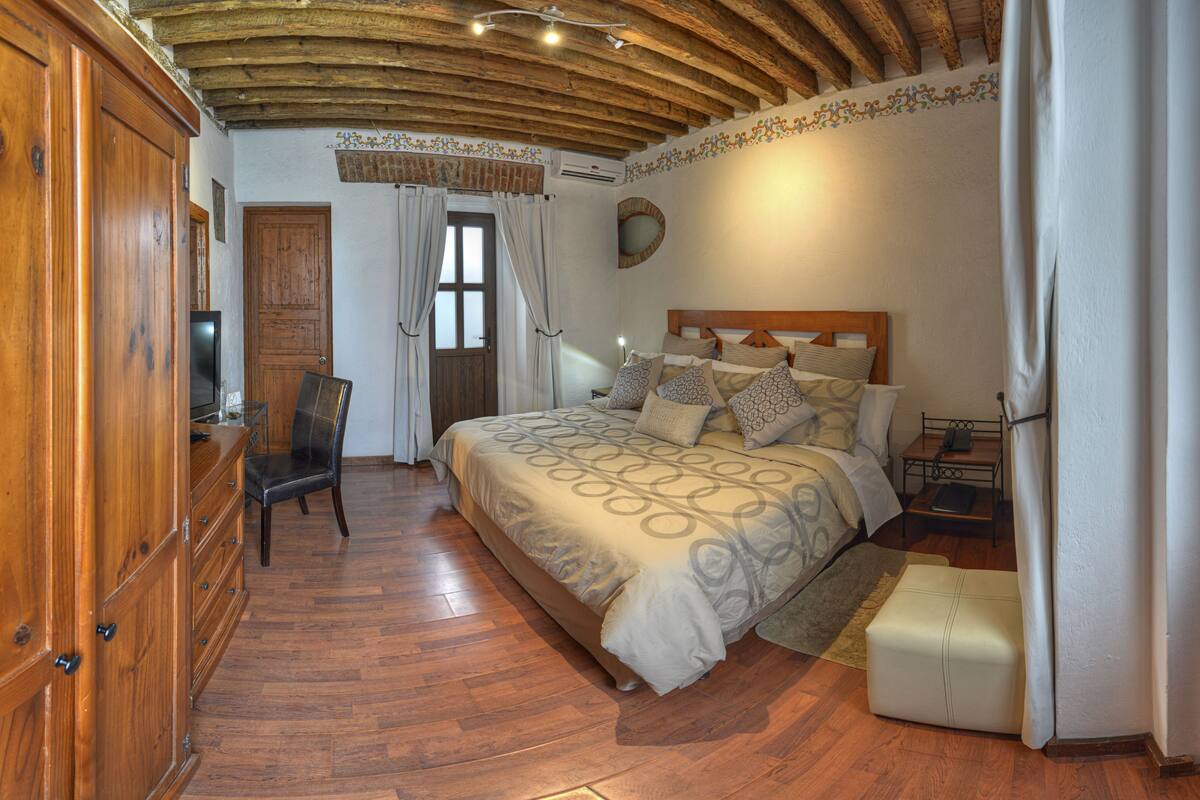 Ein Schlafzimmer mit Holzboden, einem Bett mit gemusterten Betttextilien, einem Schrank aus Holz und einem Stuhl.