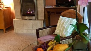 A cozy living room with a fireplace, a comfortable chair, a television, and a fruit bowl on a table.