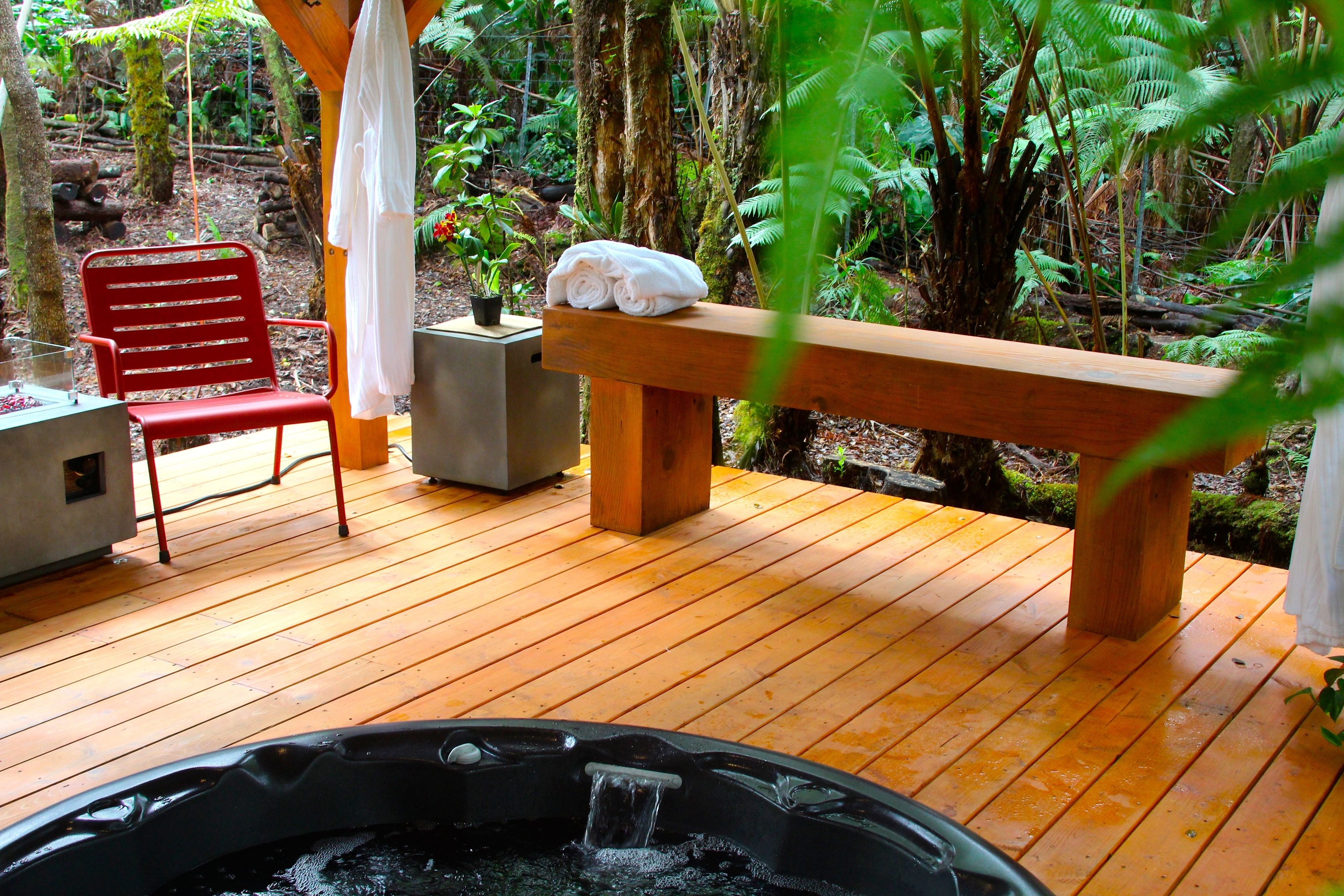 Een houten terras met een jacuzzi, een rode stoel en een bank met handdoeken.