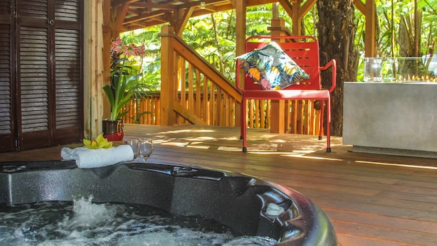 A wooden deck with a hot tub, a red chair, and a table with a glass of water.