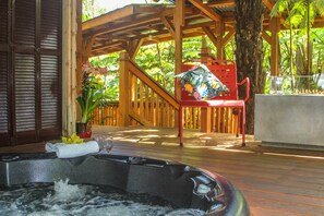 A wooden deck with a hot tub, a red chair, and a table with a glass of water. - At the Crater's Edge (Volcano)
