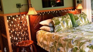 A hotel room with a bed, a small stool, a wall-mounted TV, and a decorative wall panel.