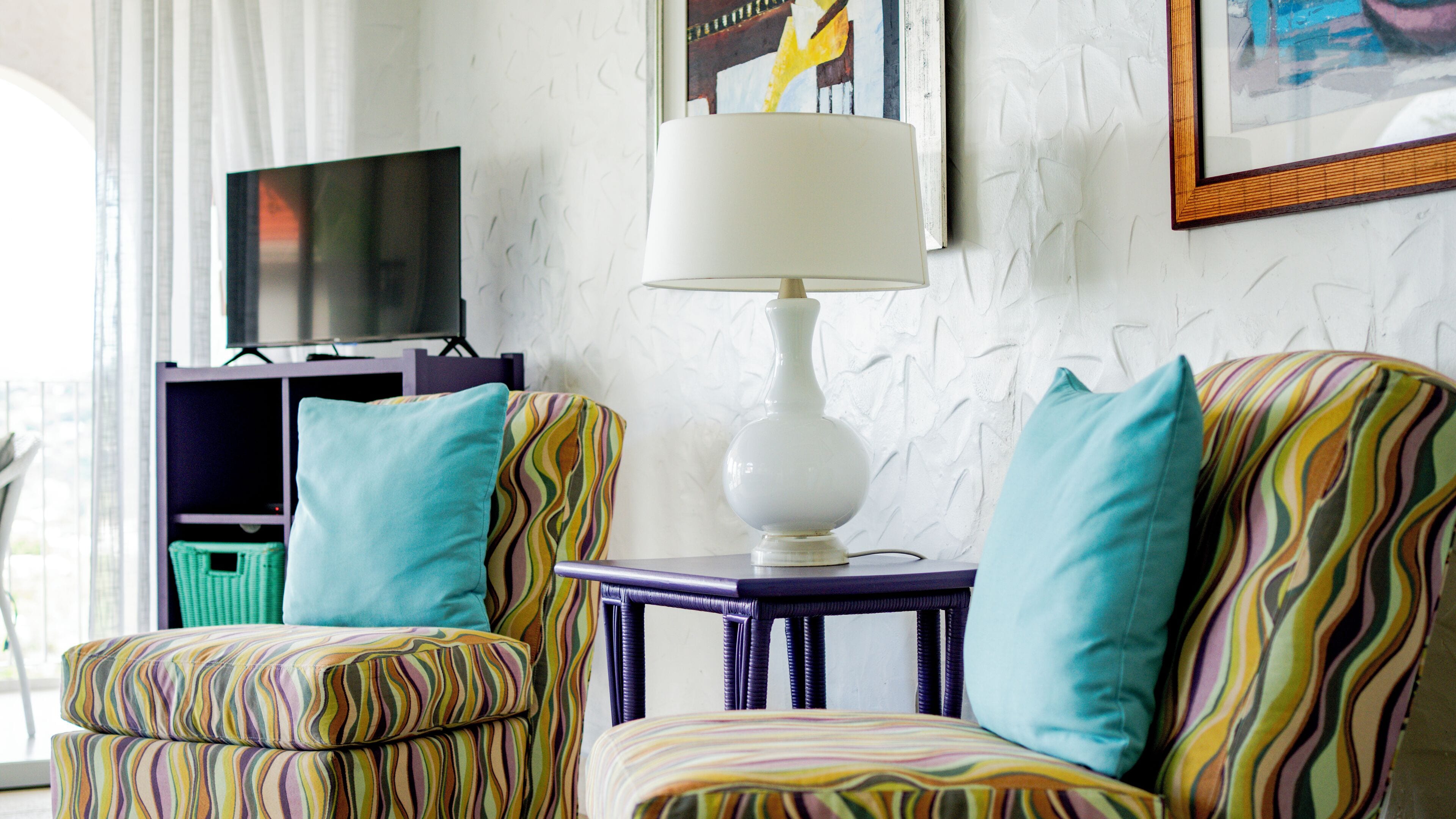 Una habitación con dos sillones a rayas, una lámpara de mesa blanca, un televisor sobre un mueble bajo y un cuadro en la pared.