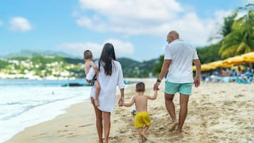 A family walking on a sandy beach with a clear sky and distant mountains.