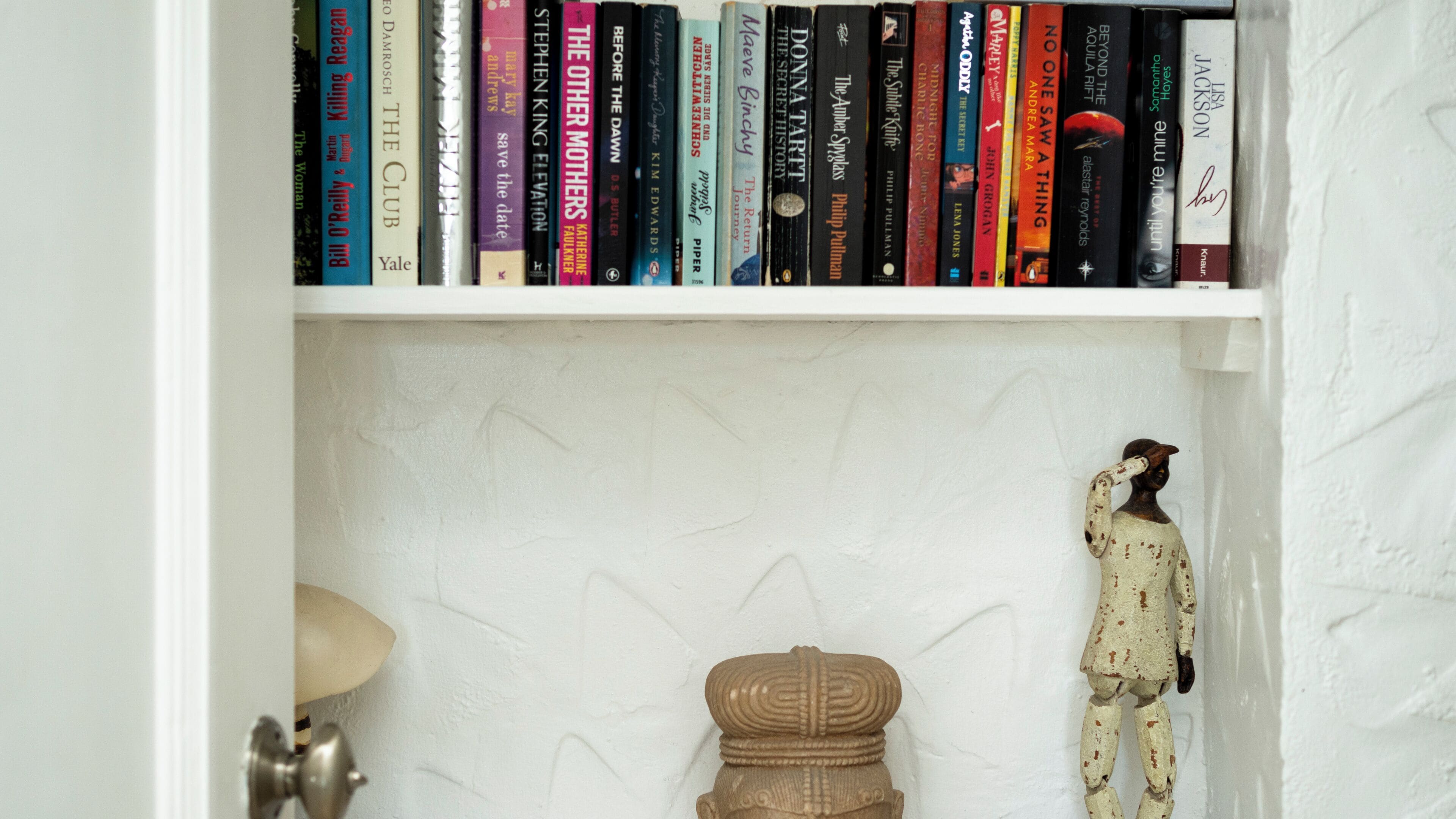 A bookshelf with a variety of books, a small decorative figure, and a lamp.