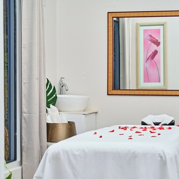 A hotel room with a bed, a white sink, a mirror, and a window with curtains.