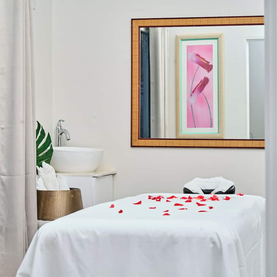 A hotel room with a bed, a white sink, a mirror, and a window with curtains.