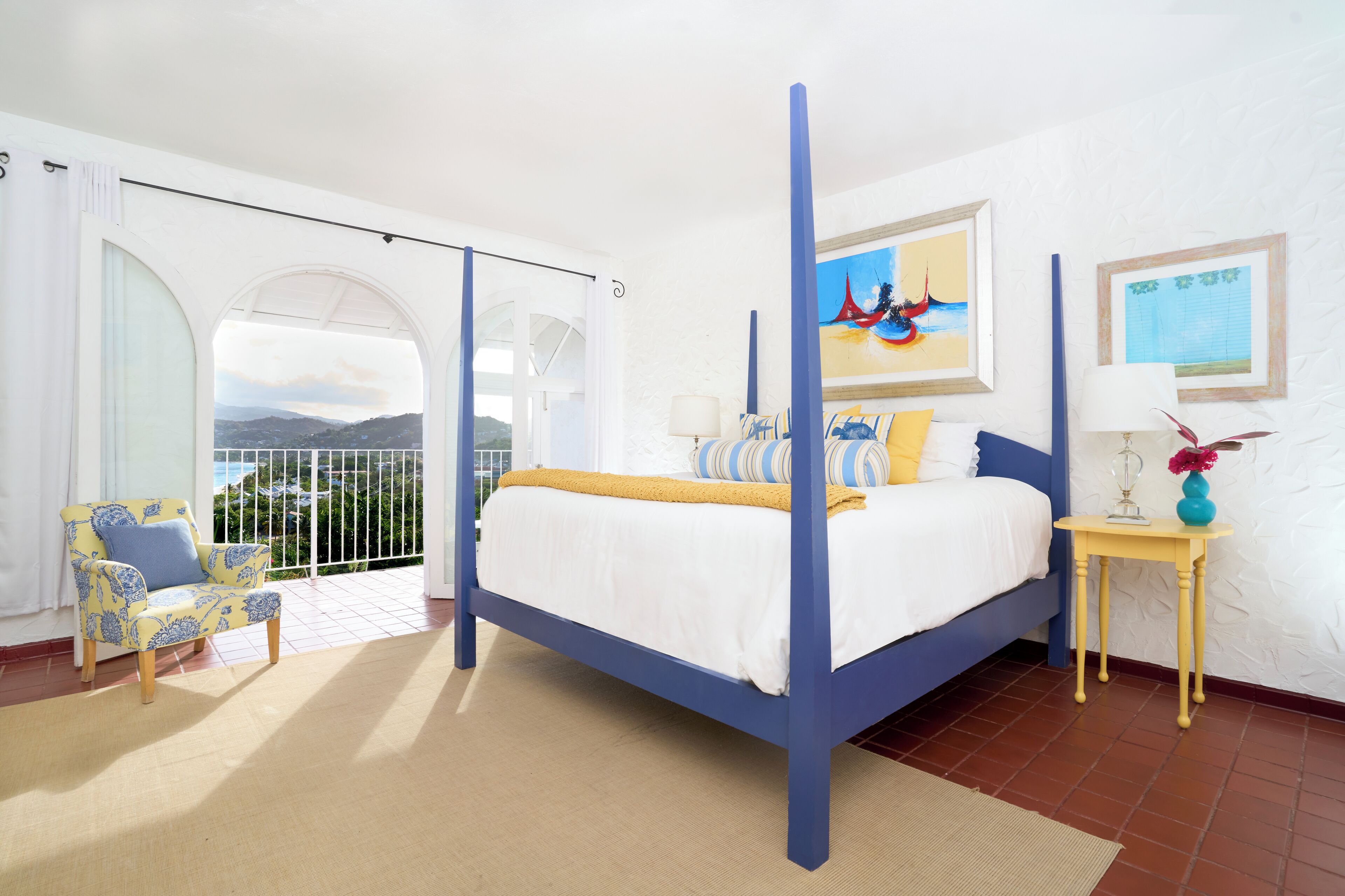 A bedroom with a bed, a chair, a small table, and a view of the outdoors.