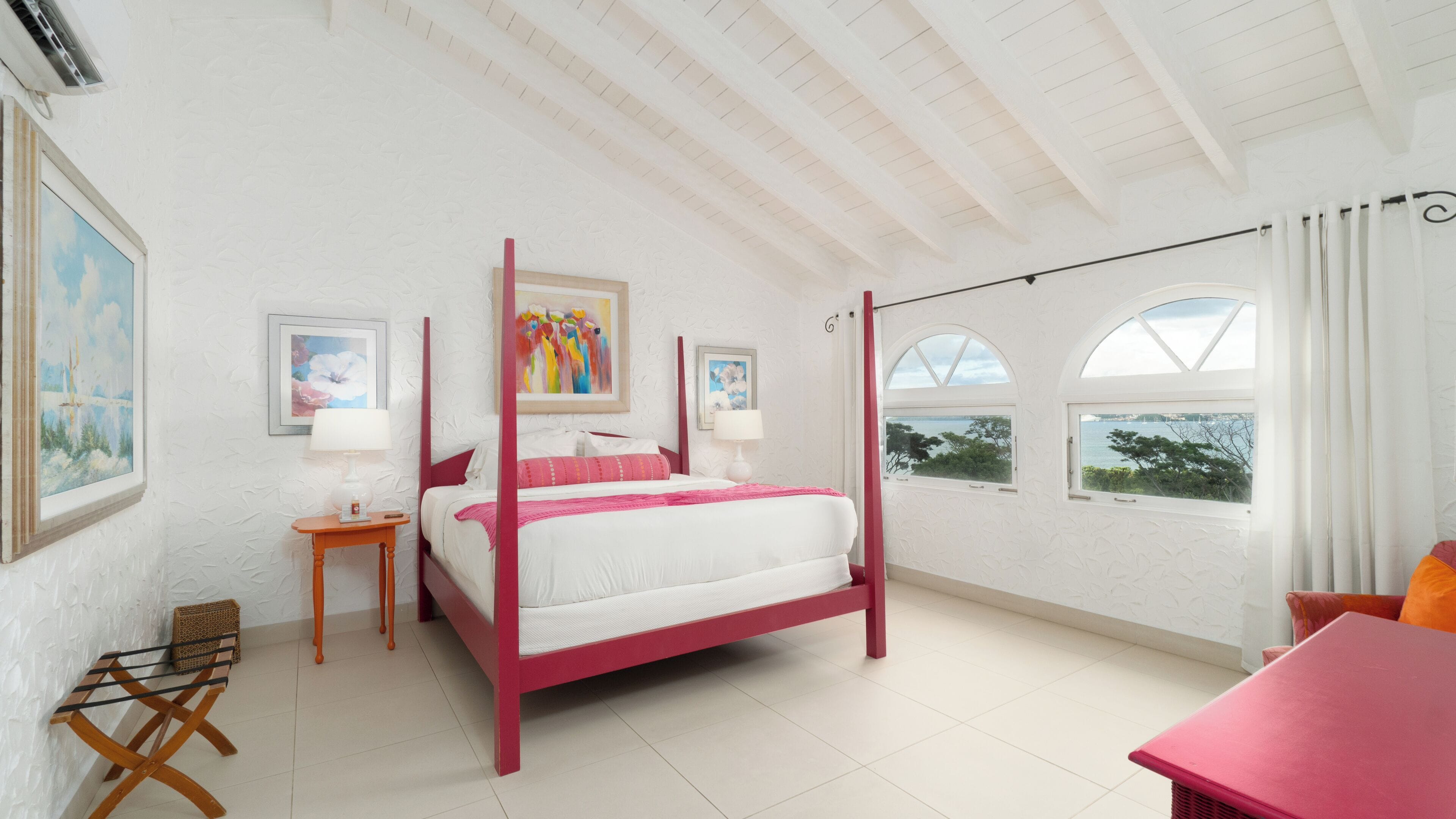 A spacious bedroom with a four-poster bed, a sitting area with a table and chairs, and large windows offering a view of the sea.