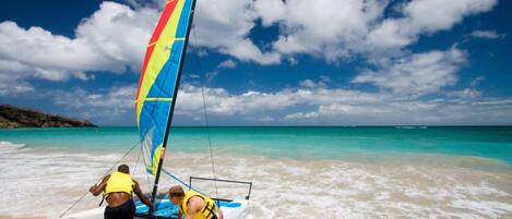 A sailboat on a sandy beach with clear turquoise water and a partly cloudy sky.