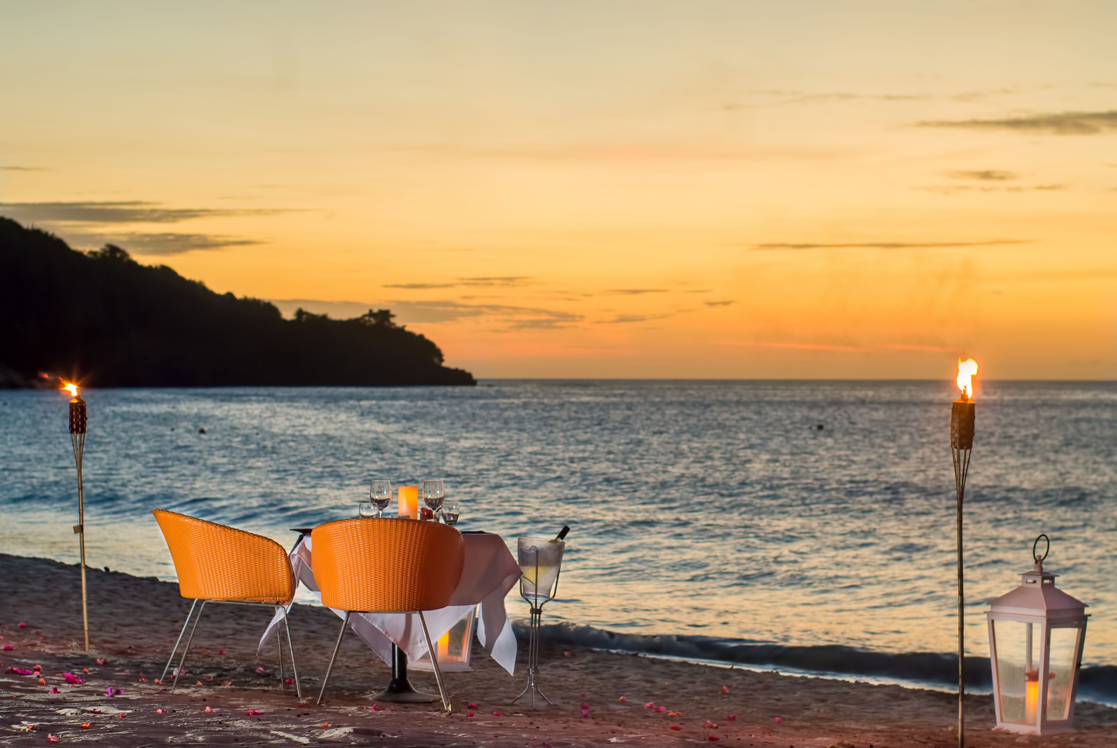 A beachside table with chairs and a candle, set against a sunset view.