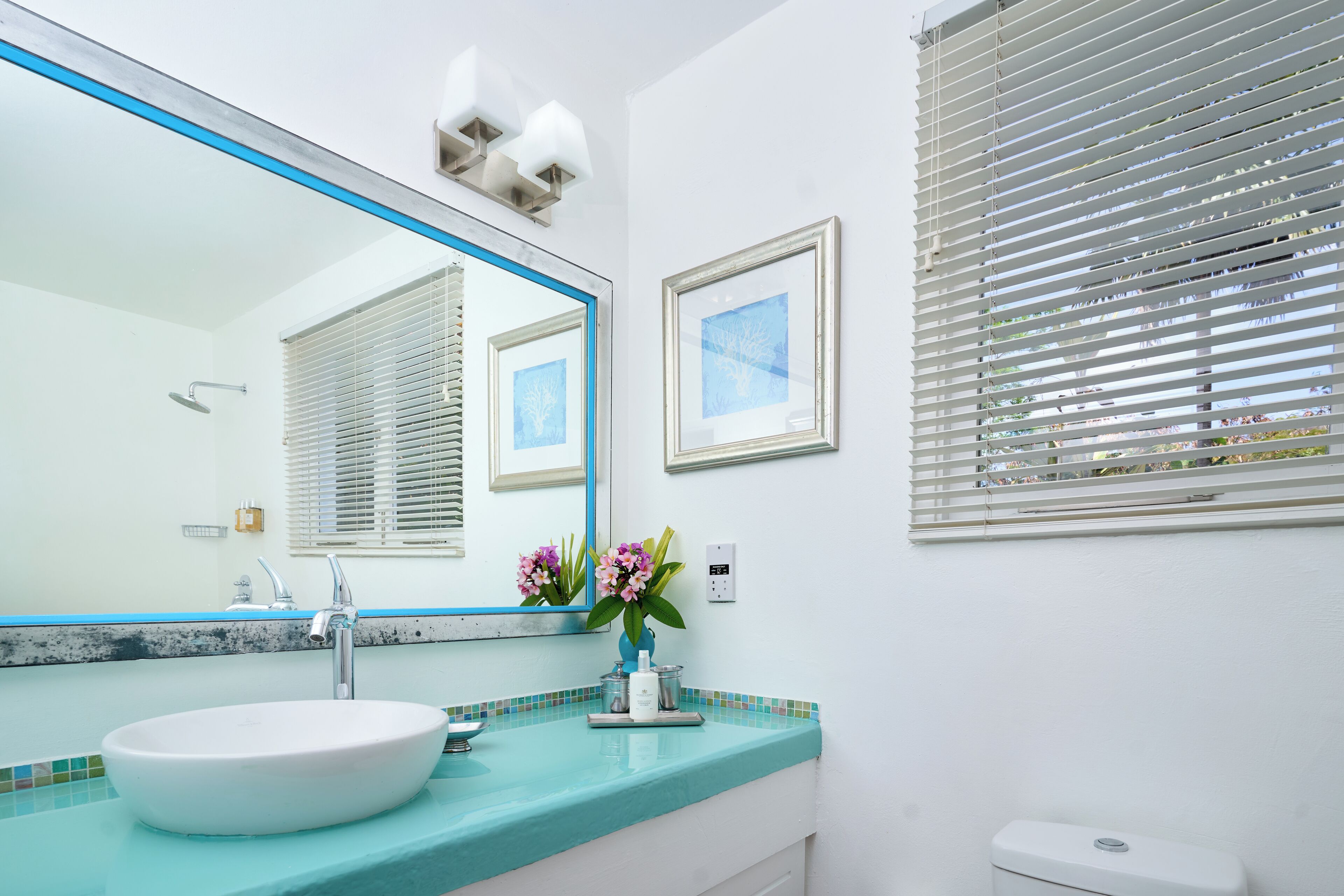 A bathroom with a white sink, a large mirror, and a window with blinds.