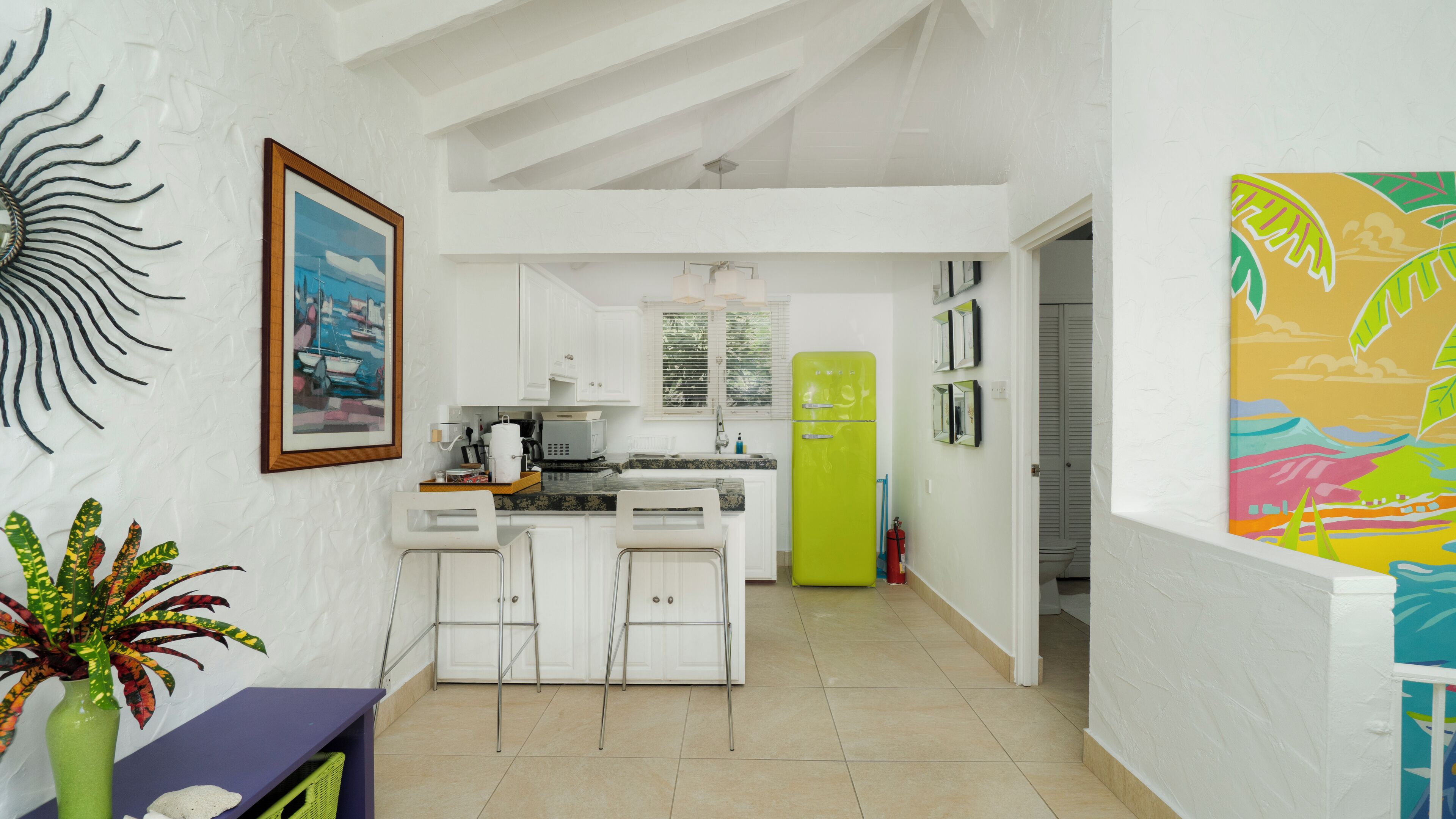 Una cocina moderna con armarios blancos, un refrigerador verde y un comedor con una silla blanca y una pequeña mesa.