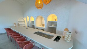 A long, white bar area with a central sink, red chairs, and overhead lighting.
