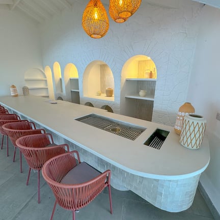 A long, white bar area with a central sink, red chairs, and overhead lighting.