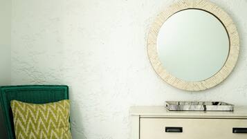 Une salle de bain avec un miroir rond, une chaise en osier verte et une commode blanche.