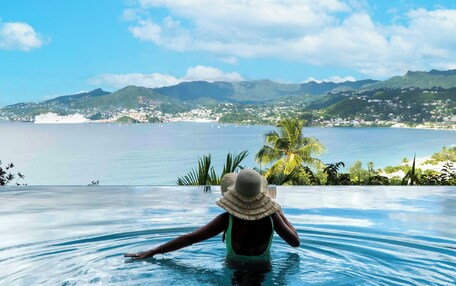 A person in a swimming pool with a view of a coastal town and mountains.