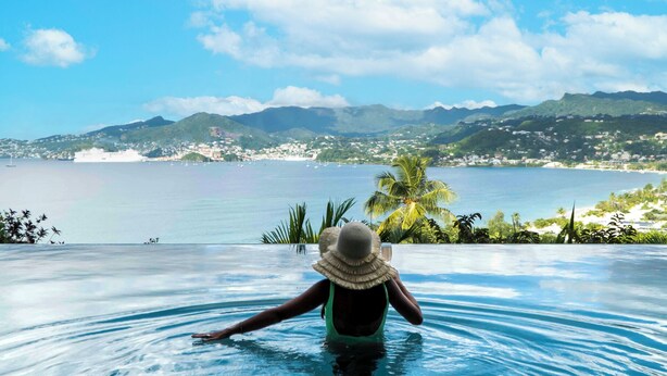 Une personne dans une piscine avec vue sur une ville côtière et des montagnes.