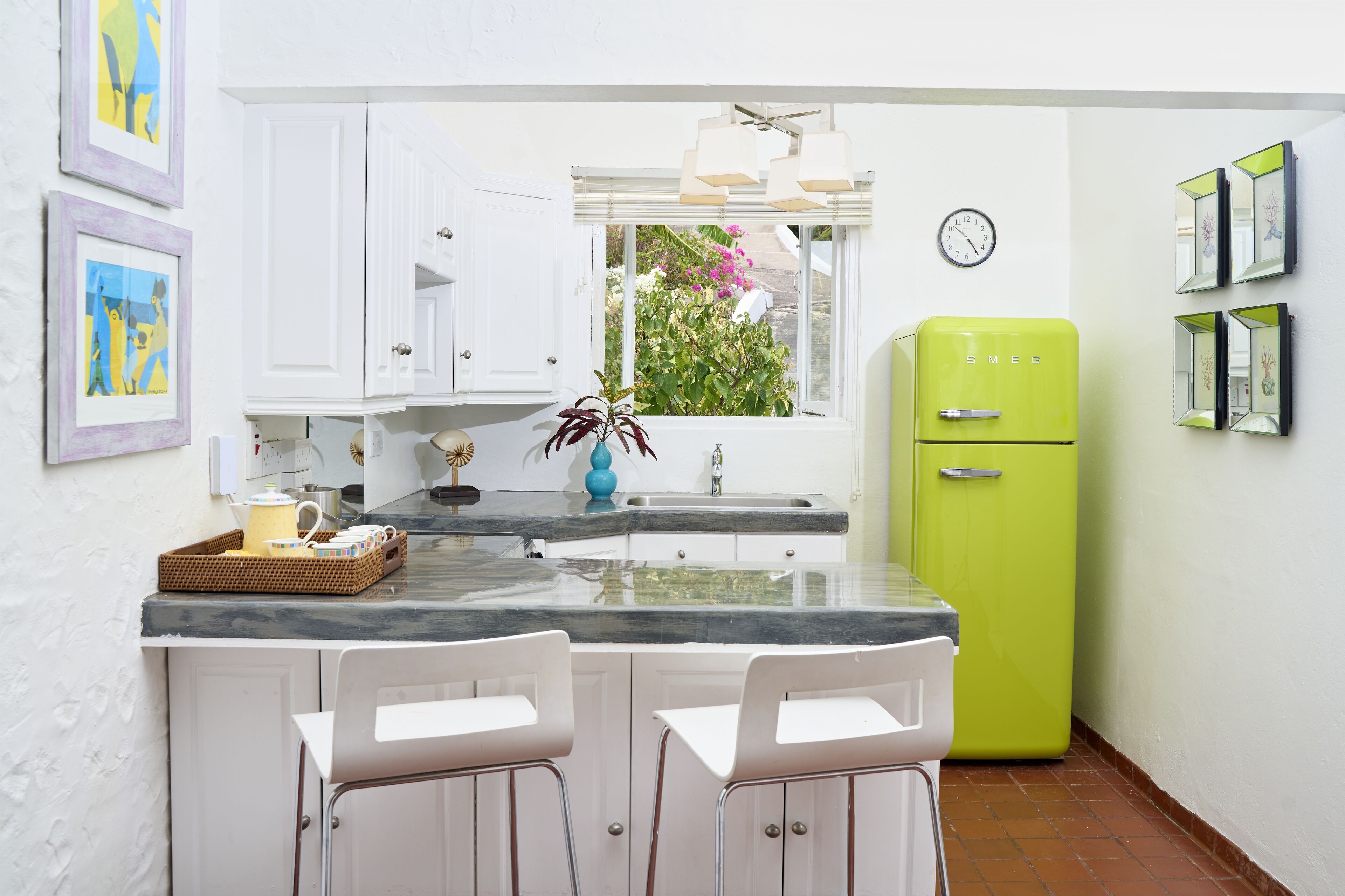 A kitchen with white cabinets, a green refrigerator, a marble countertop, and two white bar stools.