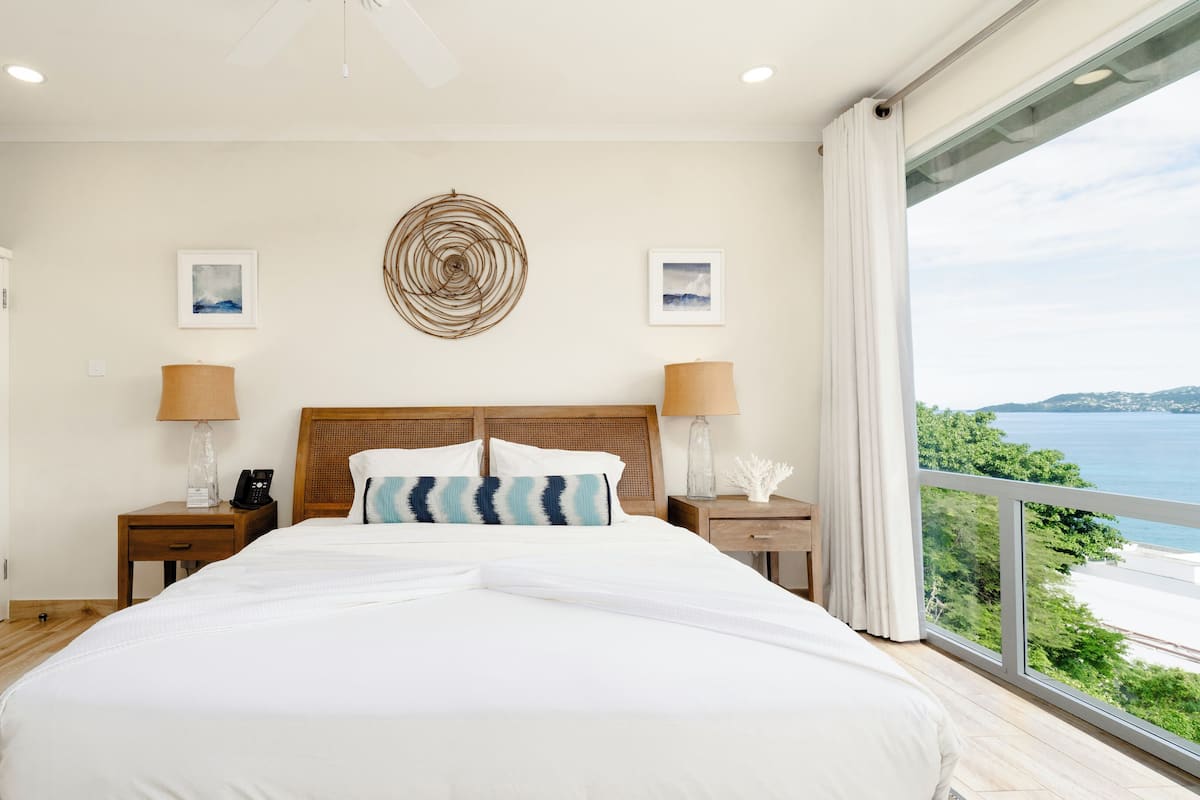 A bedroom with a large bed, wooden headboard, two bedside tables with lamps, a wall-mounted telephone, and framed artwork.
