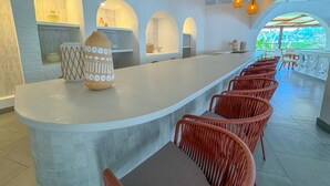 A modern bar area with a curved counter, wicker chairs, and a large decorative vase. - Mount Cinnamon Beach & Wellness Resort (St. George's)